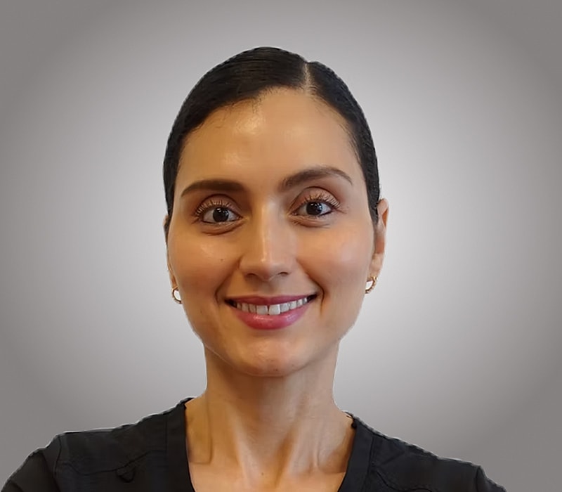 Smiling woman in scrubs against gray background.
